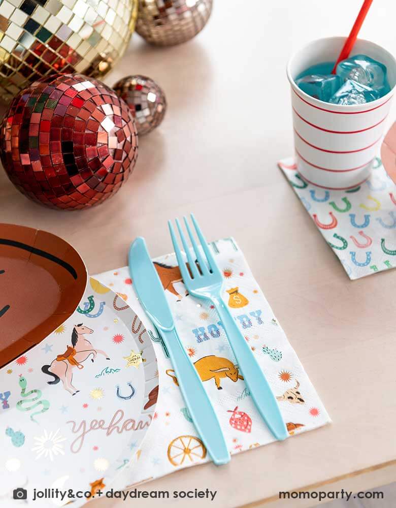 A closeup shot of a western cowboy themed party table tablescape featuring Momo Party's cowboy themed tableware by Jollity Co. and Daydream Society including the round cowboy icon patterned round plate, the large cowboy napkin, the small horseshoe napkin and cowboy hat shaped plate. With gold and red disco ball decorations on the table, making this a modern yet fun tablescape for kid's rodeo, Western or cowboy themed birthday celebration. A perfect inpso for kid's "First Rodeo" first birthday celebration.
