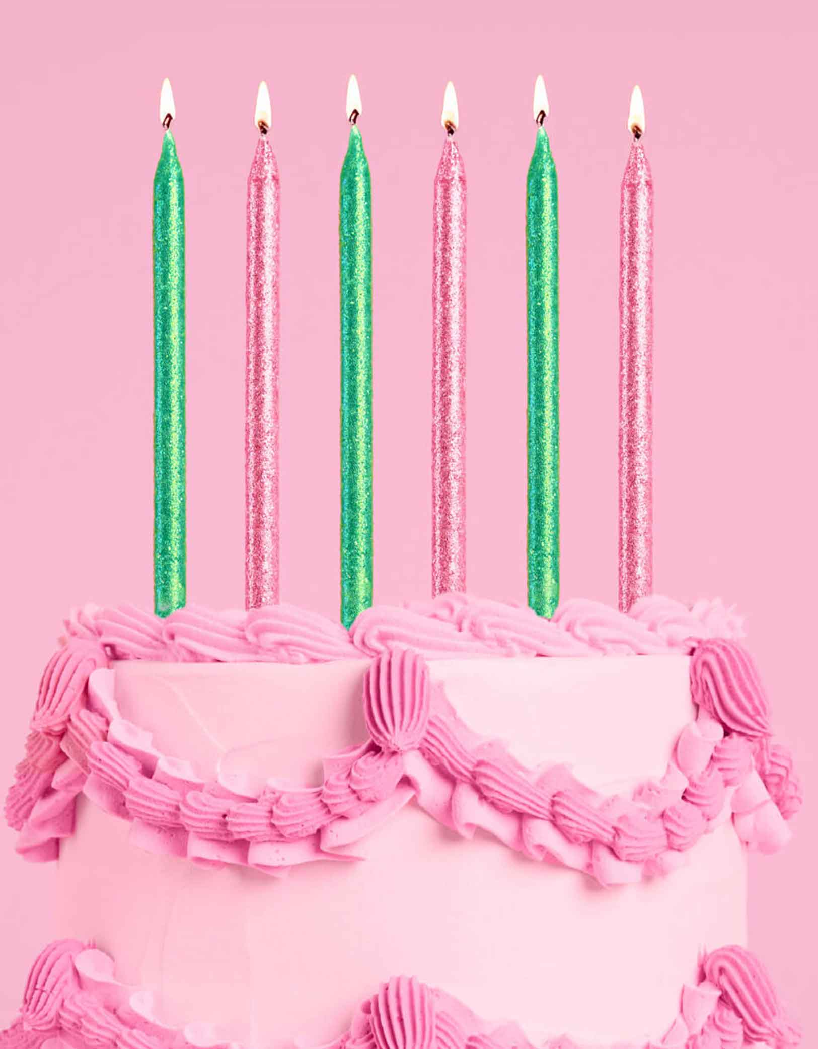 A pink buttercream cake with Momo Party's Wicked Party Emerald City Glitter Candles in pink and green by Xo, Fetti on a pink background.