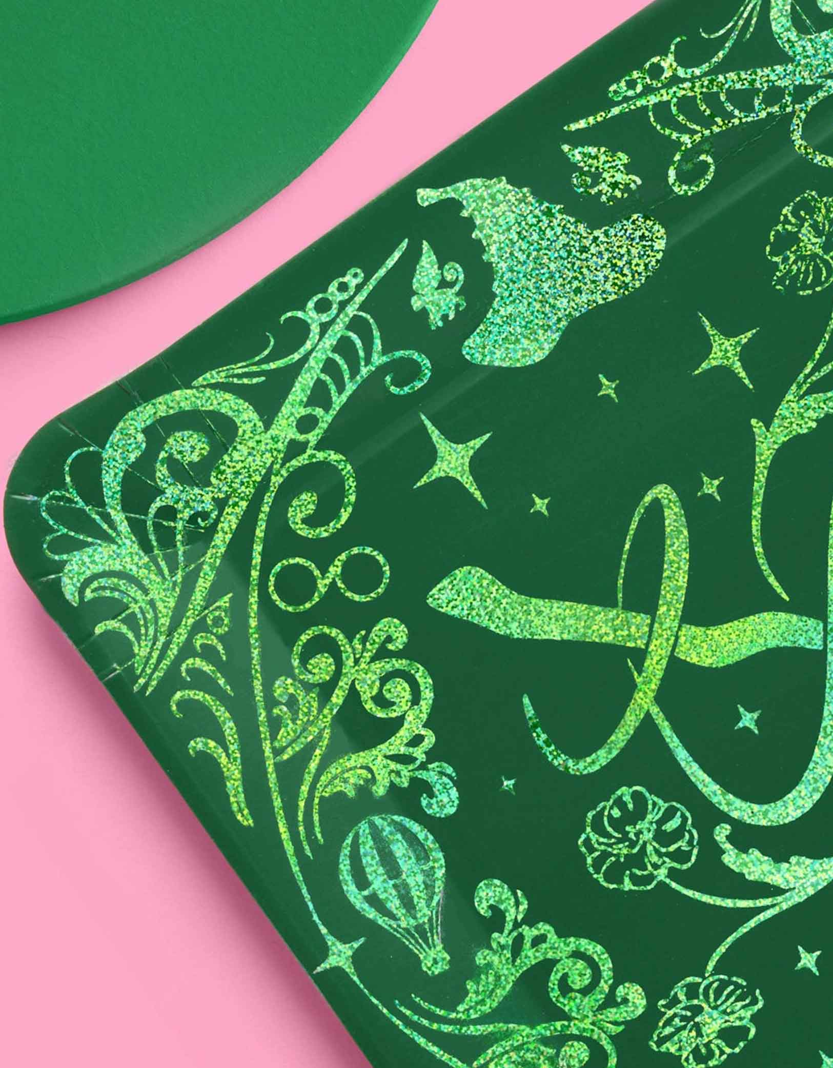 Momo Party's 10.5" Wicked party dinner plates in green with intricate wizard and Elphaba inspired designs in glitters on a pink background.