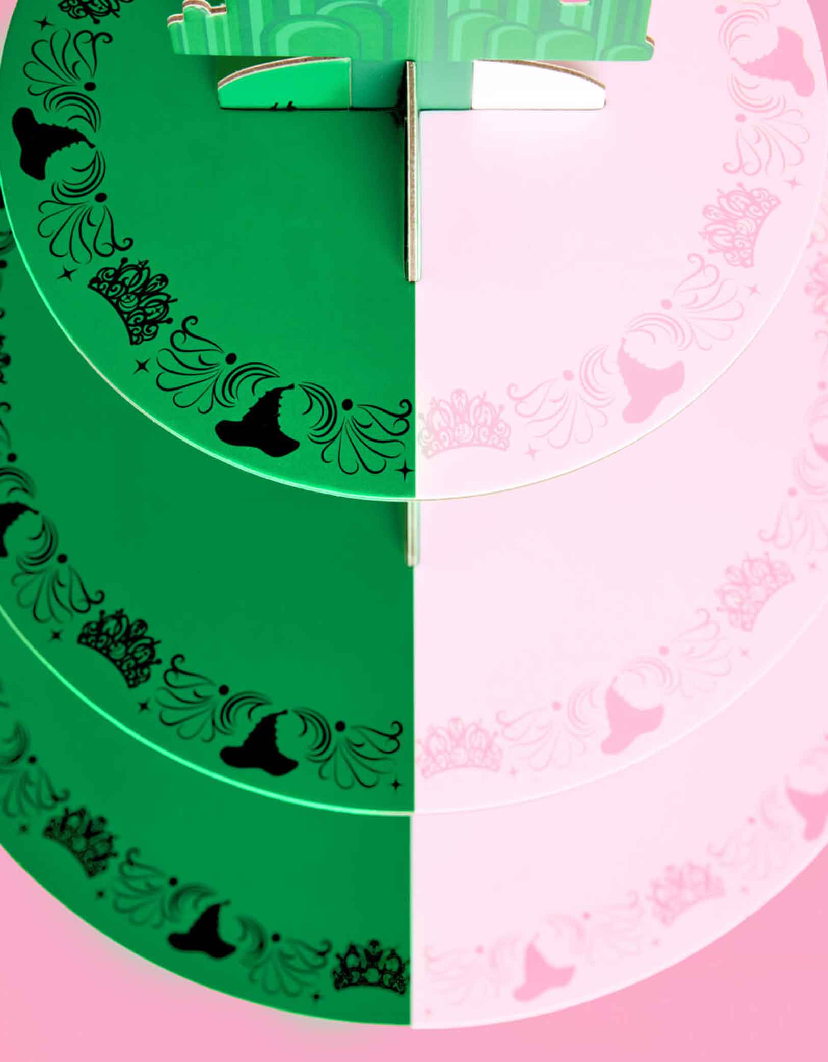 A close up shot from the top of Momo Party's green and pink cake stand with Wicked's Emerald City design at the top on a pink background. Inspired by the enchanting world of the Wicked Witch, this green and pink centerpiece adds a whimsical flair to any celebration. Perfect for showcasing your sweet treats, it transforms your dessert table into a dazzling scene straight from the Emerald City.