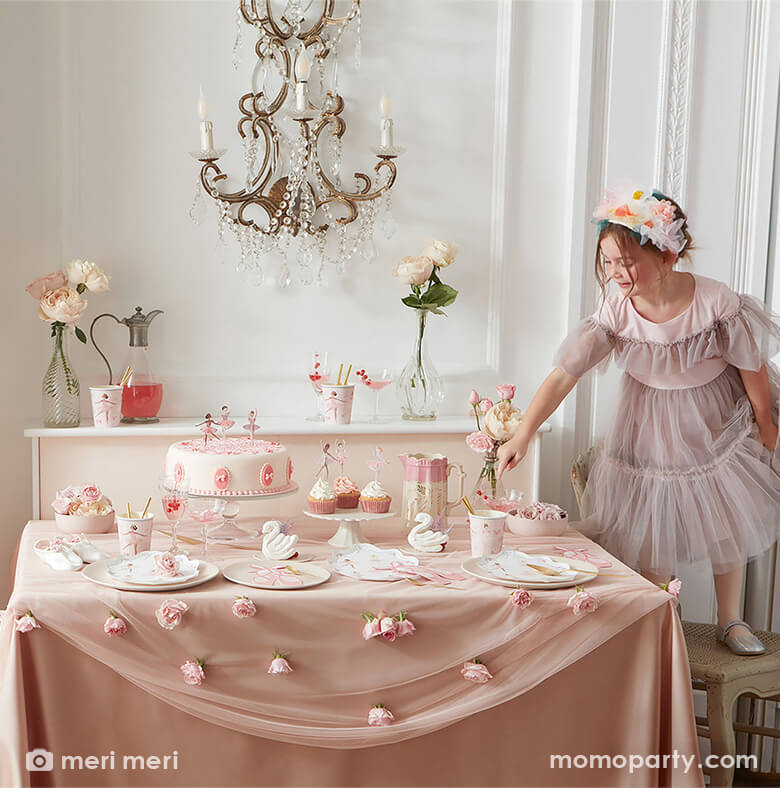 Ballet themed birthday party table setting allet themed birthday party table setting with a little girl in a lace dress and ballet shoes standing on a chair pointing to a plate full of Ballerina Plates from merimeri, Ballet Slippers Napkins, tissues, Ballet paper Cups, cupcakes and cupcakes with cupcake toppers from Ballerina Cupcake kit, flowers, swan decorations, all on a pink and flesh toned silk tablecloth. Such a modern and dreamy ballet themed birthday party