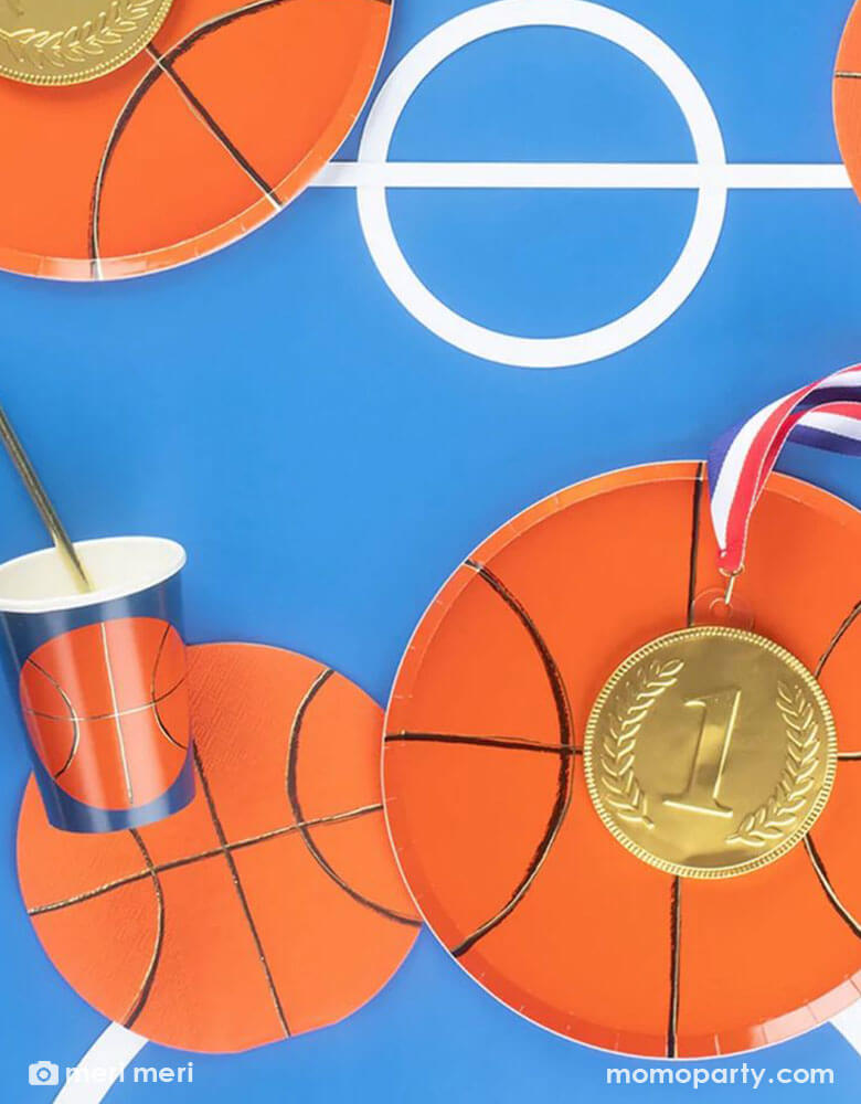 A table set with basketball themed tableware from Momo Party including a 8" basketball shaped plate, 6.5" basketball shaped napkin and a 9 oz basketball party  party cup by Meri Meri.