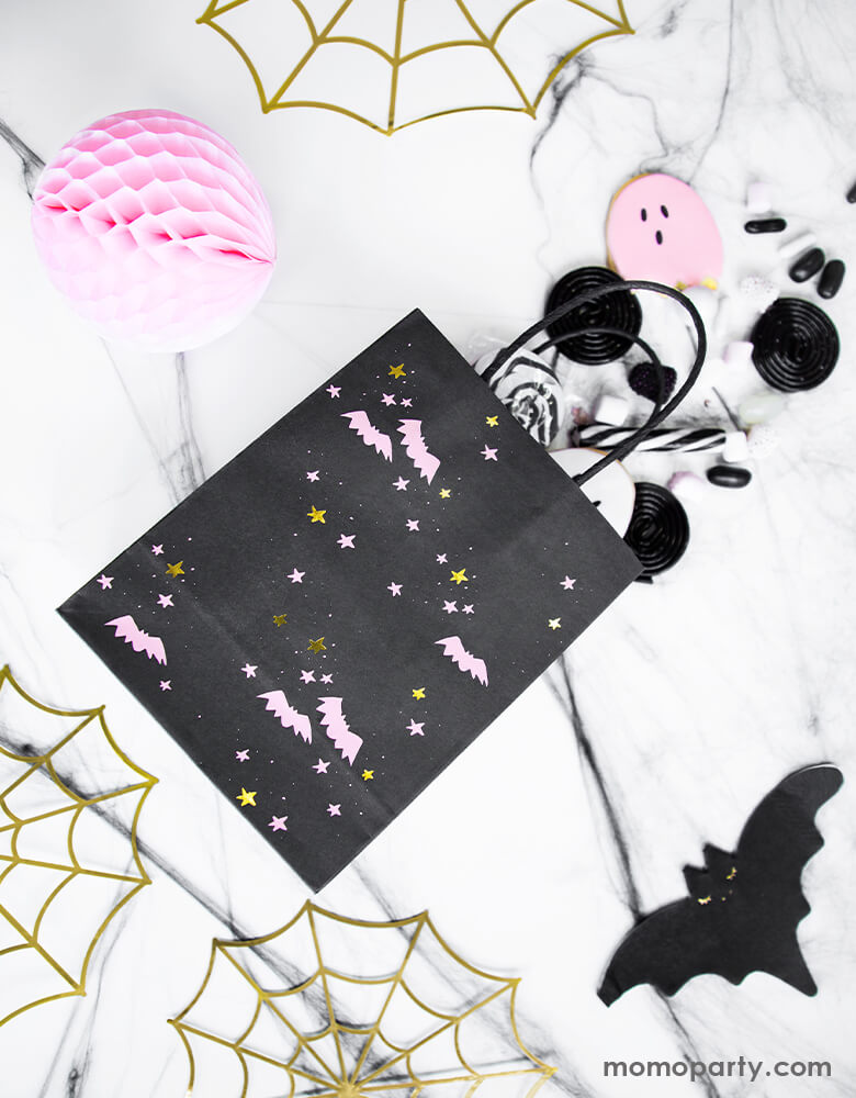 A kitchen table top filled with candies, pink ghost cookies come out from a Halloween Bats Black and Pink Party paper Bag, a pink honeycomb decoration, Bat napkins and gold spider web decorations around it. These modern high quality party supplies are prefect for Kids Not-so-scary Halloween party, hocus pocus party, trick-or-treating party, spooktacular halloween party and all halloween related celebrations. On sale at party online store, party boutique online store, party supplies at momoparty.com