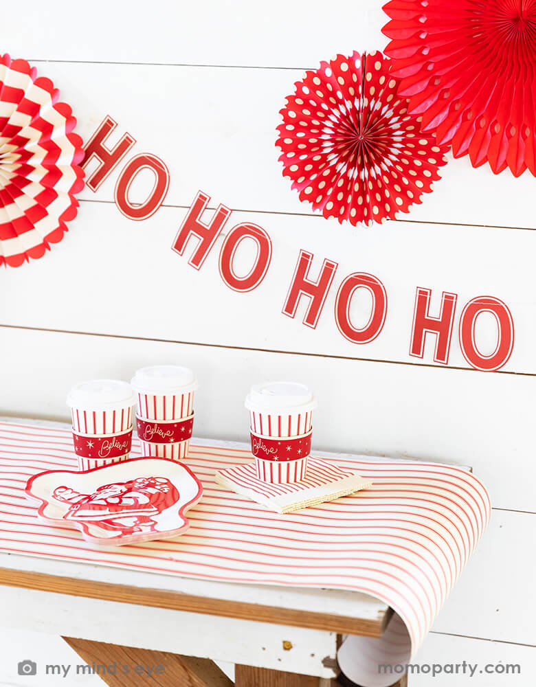 Holiday home decoration with ED STRIPE COZY CUPs and BELIEVE 9" SANTA PLATE over the Believe Christmas Red Striped Table Runner. And Believe Ho Ho Ho Banner and Believe Christmas Paper Fans hanging on the wall. Modern and stress free holiday party supplies from momoparty.com