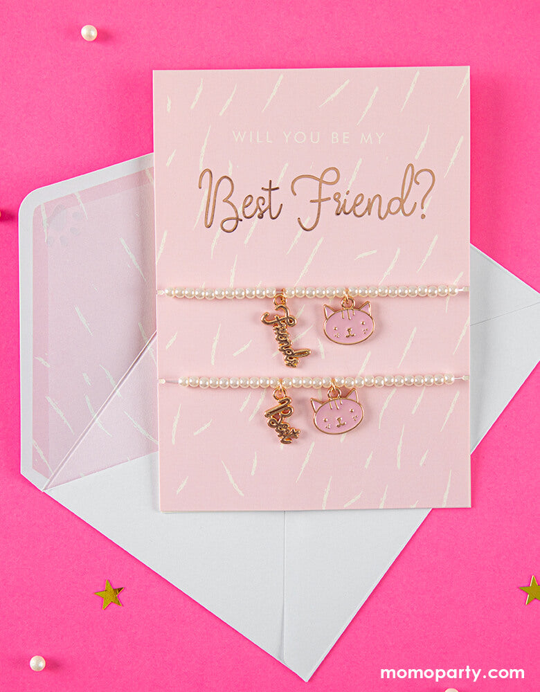 Party Deco Best Friends Bracelets Card with its adorable envelope on a bright pink background. featuring two bracelets with pink kitty pendant and "best" "friend" word pendant in gold on a card. This adorable card with two kitty cat bracelets comes with a cute envelope. It's perfect for your little one's Valentine's exchange!