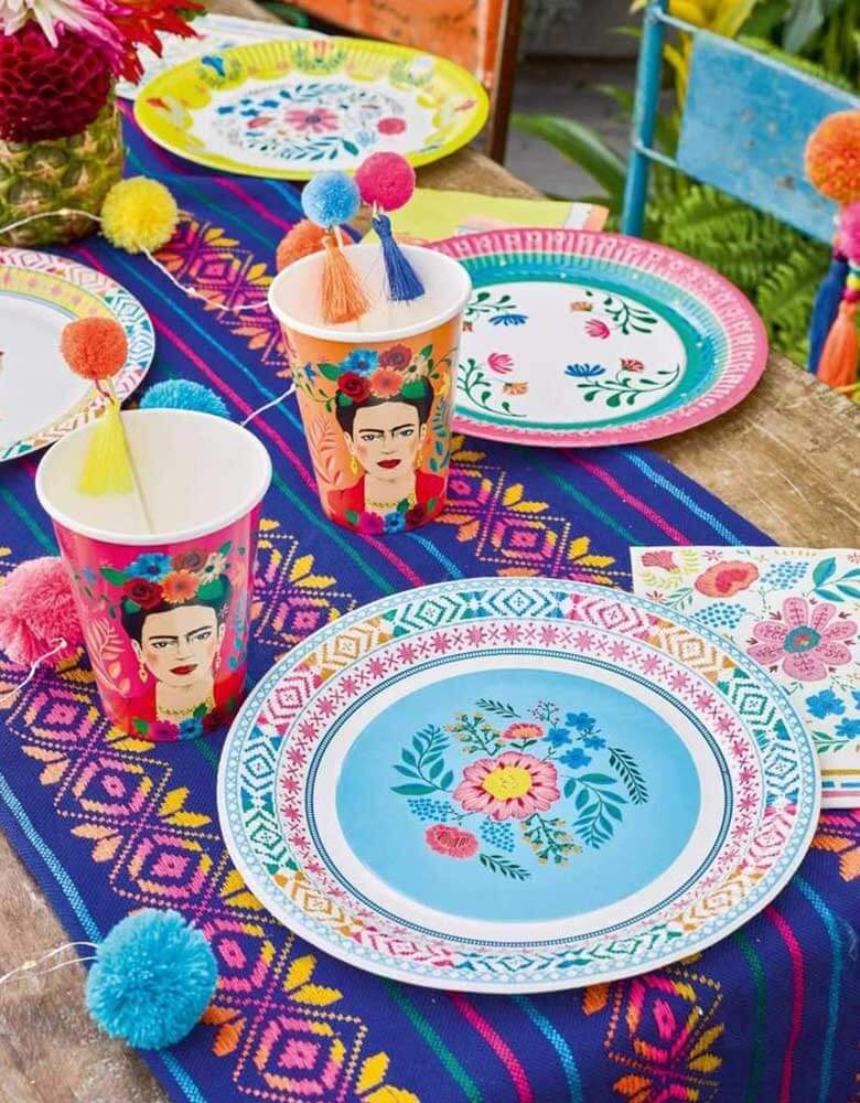 A Boho Fiesta Themed Party Table featuring Talking Tables 9" Boho Fiesta Floral Plates and Napkins with treats and pom pom food picks with a Mexican blanket beneath it