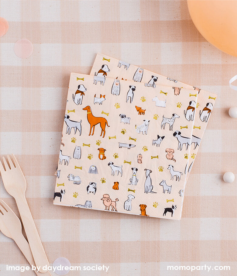 Flat lay with Bow Wow Large Napkins from Jollity & Co Party Boutique - Daydream society- Bow Wow collection. Printed with variety breed of dogs in morden illustrations with a warm neutral color palette and gold foil elements, and wooden utensils, blush latex balloon, confetti on top of Natural Cabin Check Tablecloth. These puppy dog party ware are definitely best for a pet lover party, dog lover party, pets party!