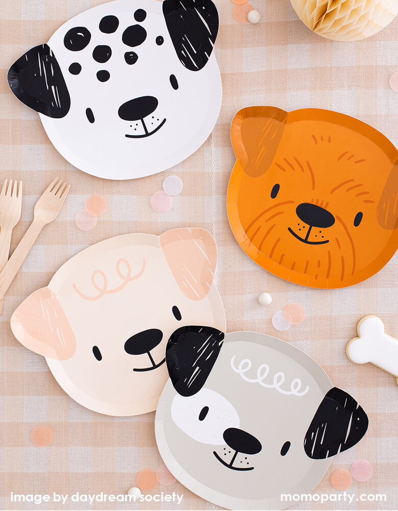 Party Boutique - Daydream society- Bow Wow collection. Featuring cute dogs head shaped paper plates of 4 designs in morden illustrations with a warm neutral color palette, with wooden utensils, light colored confettis on top of Natural Cabin Check Tablecloth. These modern Dog Birthday Party Supplies are perfect for a dog lover, a dog themed birthday party, Let's Pawty birthday party, adorable puppy themed party