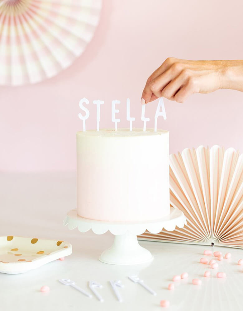 My Mind's Eye Cake By Courtney White Letterboard Cake Toppers on a pink cake with pale pink paper fans on the wall as decorations