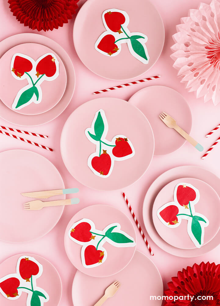 A pink and red themed party table styled with pastel pink round plates layered with party deco's cherry shaped die-cut napkins featuring gold details, along with pink and red party fan decorations and red striped party straws spread out the table, , makes a simple party idea and inspiration for a girly Valentine's celebration or Ganlentine's Day party with your BFFs