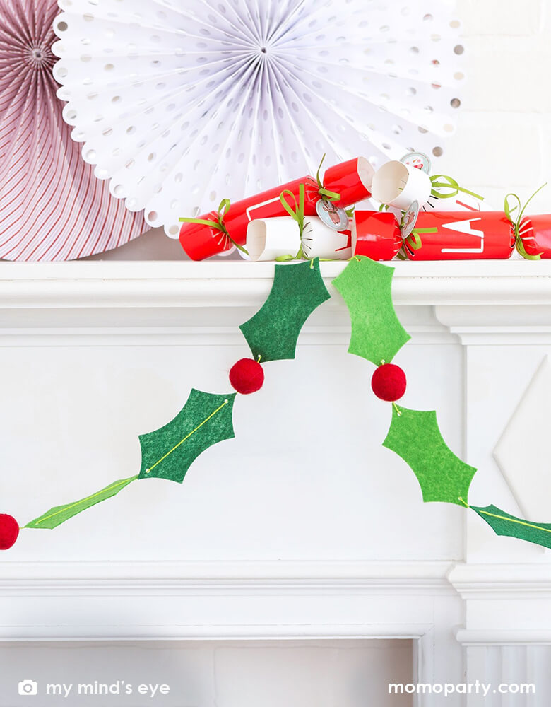 Close up of Christmas Metal decoration, with My Mind's Eye Holly And Berries Felt Banner with 26 Holly leaves and 10 felt balls hanging on the mental, Fa la la crackers and paper fan on the top, it makes modern and cozy Christmas gathering. Perfect to line the food table at your Christmas party. Adorn your Christmas tree with this festive felt garland.