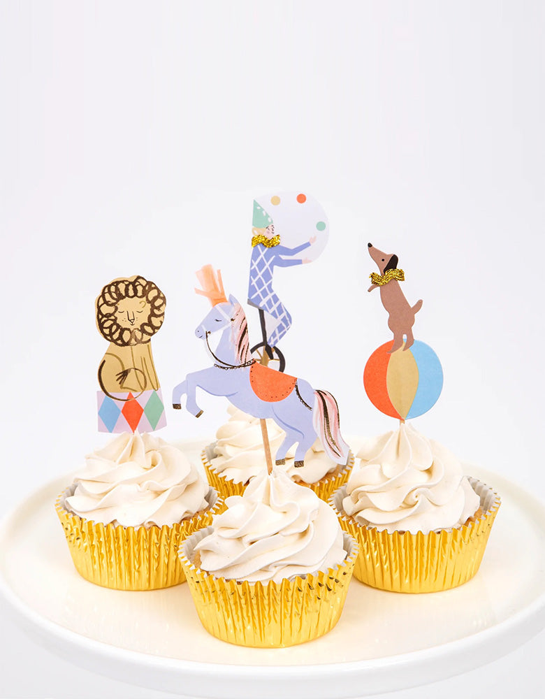Momo Party's Circus Parade cupcake kit by Meri Meri, comes in a set of 24 fantastic toppers with 4 circus designs, including horses with paper tassels on their heads, a circus dog on a bounce ball, a lion and a circus juggler, and 24 shimmering gold foil cases.