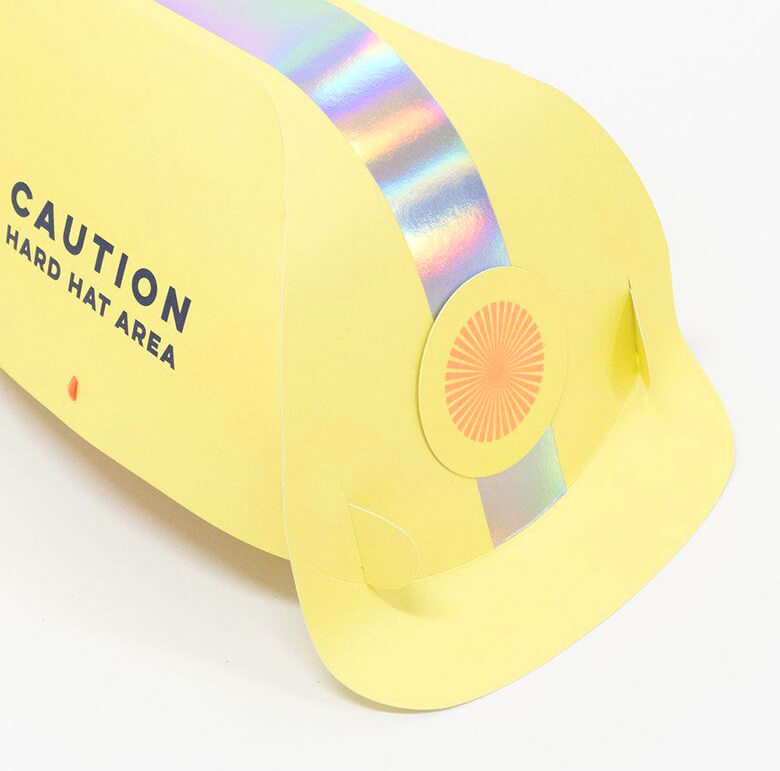 close up details of Meri Meri Construction Party Hats. They are crafted from high quality card and feature the words "Caution. Hard Hat Area" in the side of the hat. They have lots of shiny silver holographic foil for a fabulous effect, They are comfortably kept in place with bright orange elastic