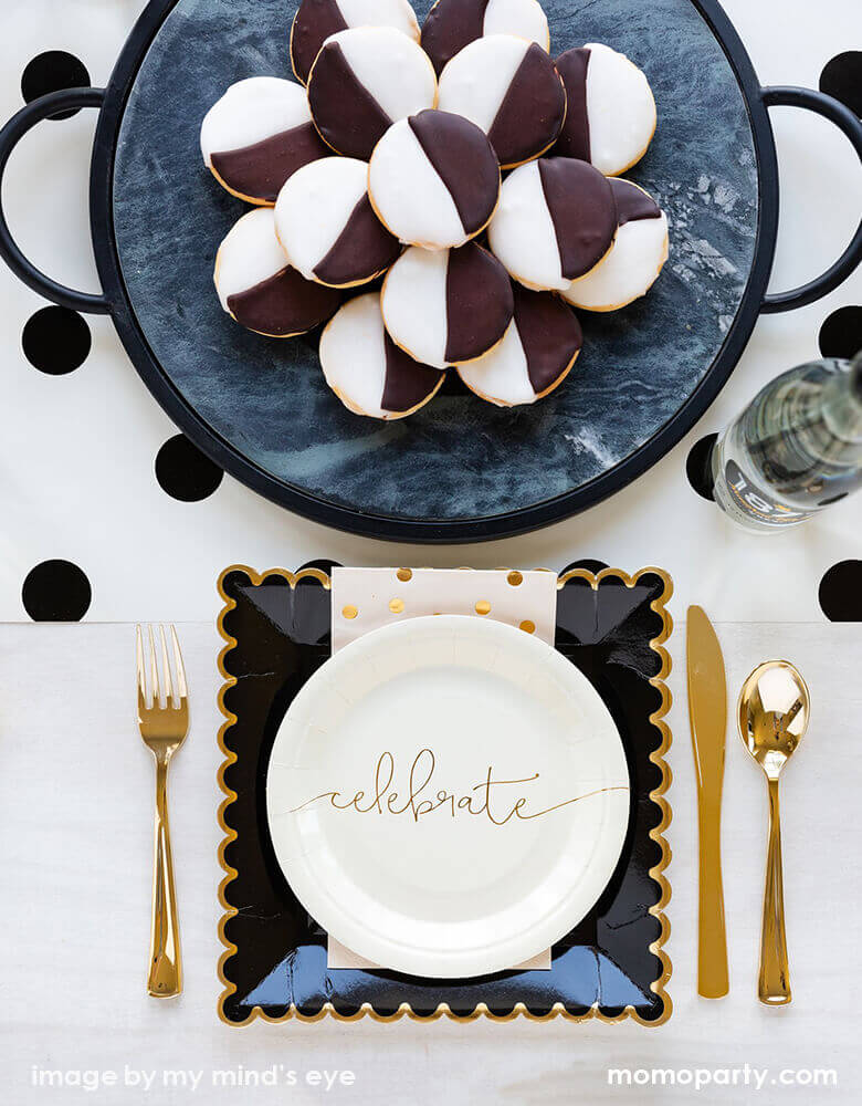 Modern celebration table top, setting with my mind's eye Cheers small Plates layed with Black Scalloped Large Plates and gold polka dot napkins, with golden cutlery on the side, a glasses of drink, and sweets on a black tray on top of Cream with Black Dots Table Runner in the table center. These simple elegant partywares make your every celebration in styl