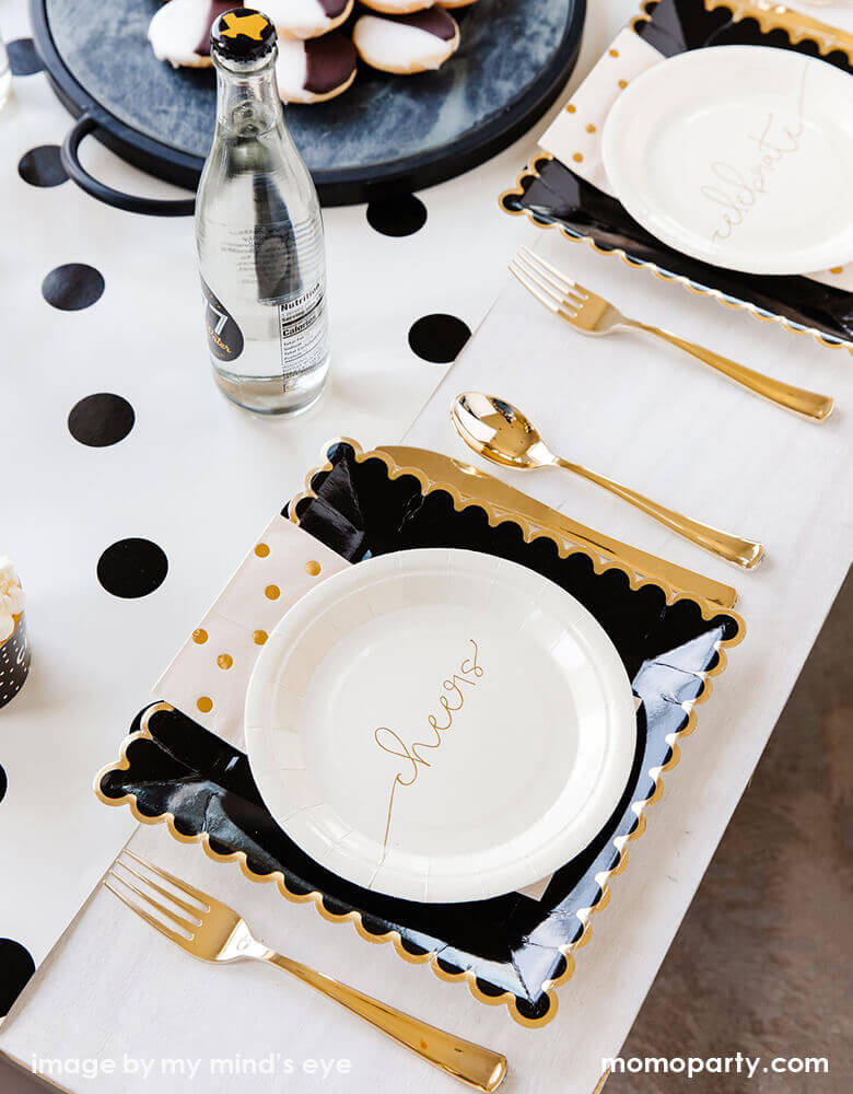 Modern celebration table top, setting with my mind's eye Cheers small Plates layed with Black Scalloped Large Plates and gold polka dot napkins, with golden cutlery on the side, a glasses of drink, and sweets on a black tray on top of Cream with Black Dots Table Runner in the table center. These simple elegant partywares make your every celebration in style