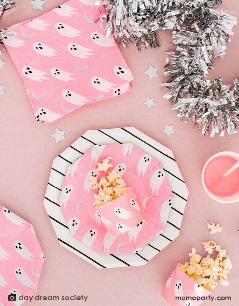 A pink party table with Daydream Society_Halloween Spooked Party Supplies with adorable ghost design on a neon pink background, along with sliver star shaped confetti and silver streamer, a perfect table scape inspiration for a kid's friendly not-so-spooky Halloween celebration 
