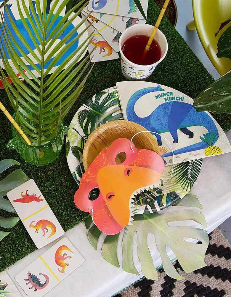 A kids dinosaur themed birthday party table filled with Talking Tables' Party Dinosaur collection including dinosaur masks, party cups, games and tableware
