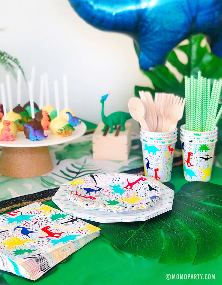 Kids Modern Dinosaur Party Table Set up with Neon Dinosaurs graphic paper plates, napkins, cups, wooden utensil, paper straw, dinosaur cake pop  