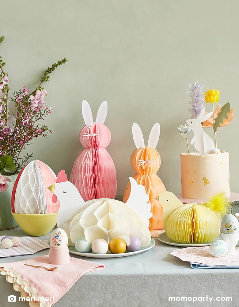 Easter kitchen table set up with Meri Meri Easter Honeycomb Decorations with a Hen laying on a plate with colorful eggs under it, a stripe egg honeycomb on a yellow bowl, 2 bunnies honeycomb decoration stand next to a white buttercream cake decorated with Easter Cake Toppers, fresh flower in a vase, floral paper plates and Gingham napkins. Super adoration and unique party decoration for Easter party