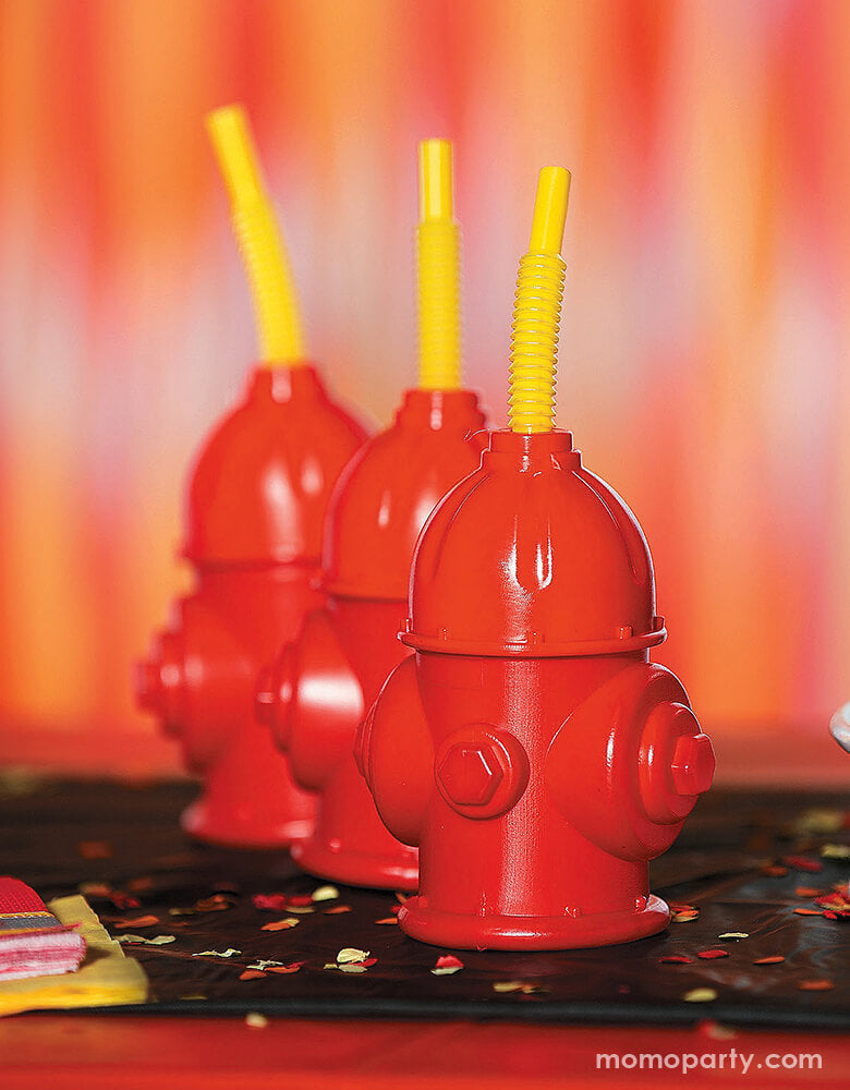 A close up look of firefighter birthday table with three Fire Hydrant sipper Cup with straw on the table with red and yellow confetti