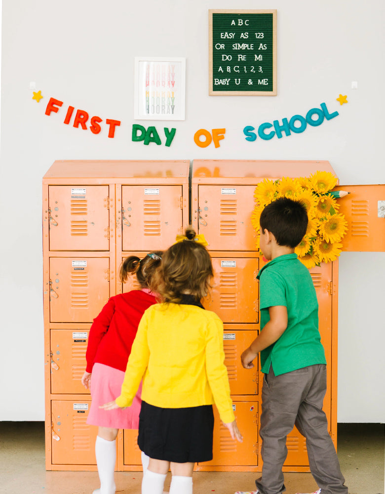 Kids standing in front of vintage school tin cubby with studiopep's hand stitched first day of school felt banner in bright and vibrant colors to celebrate the start of a new school year