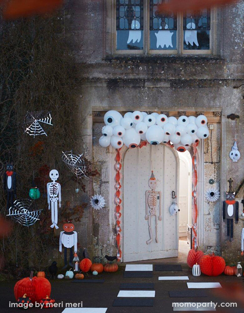 Halloween outdoor Spooktacular Decoration for a fun trick or treat, with Meri Meri Eyeball Balloon Garland hanging on the top of the entry door, Vintage Halloween Honeycomb Decorations and Halloween Hanging Cobwebs hanging on the side of the ivy wall, Halloween Honeycomb Pumpkins on the floor, hanging ghost on the window. These unique cool Halloween decorations will definitely put a smile on all your party guests' faces