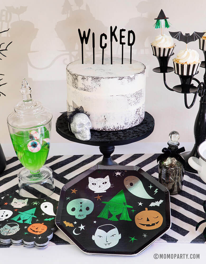 Close up look of Momo Party Halloween collection, Witch Please Party Dessert Table Set up with Meri Meri Halloween Motif Dinner Plates, napkins, cake with black letter board cake topper spelled of "Wicked", Apple jelly in with eyeball candy in a jar, Witch poisons and potions, cupcakes with Meri Meri Halloween Motif Cupcake topper on top of black candle chandelier. for a Creep cool look for A Modern Witch Inspired Halloween Party