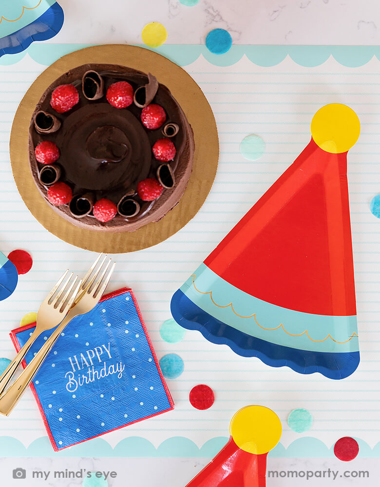 A festive birthday party table with a chocolate birthday cake, filled with cheerful confetti in blue, red and yellow and My Mind's Eye blue Happy Birthday napkins with blue birthday hat shaped party plates, a perfect combination for a boy's birthday party.