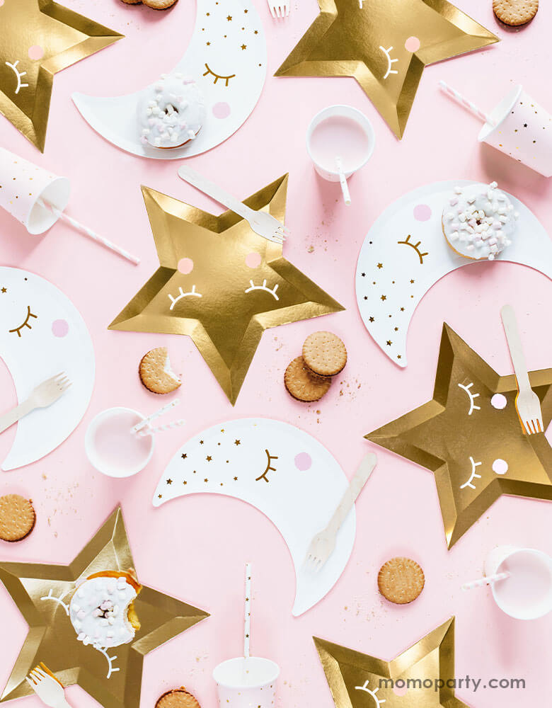 A flatlay shot of a baby pink table setup for a sweet baby shower filled with sweet Star themed party goods including die cut gold star plates, little star napkins in white, moon shaped plates in white with pink party cups