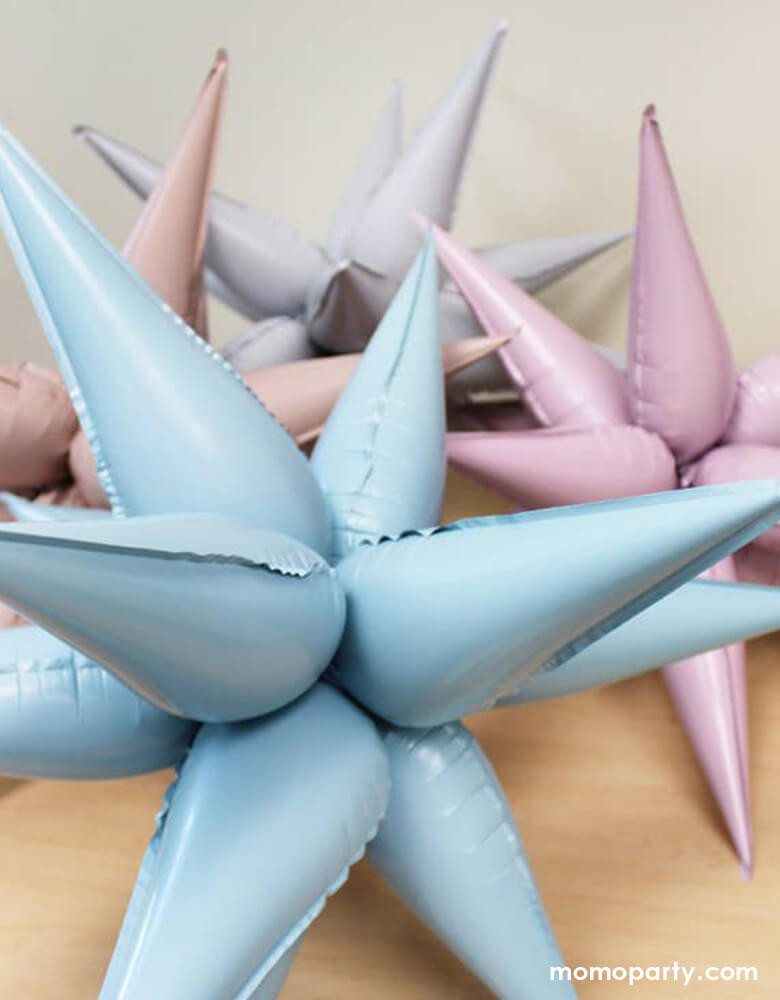 Set of 4 Momo Party's Jumbo 12 Point Starburst Foil Balloons in Blush, White, Pastel Pink and Pastel Blue colors display on the table. These 26 inches jumbo starburst foil balloons by Ellie's Party are simply a show-stopper for any celebration
