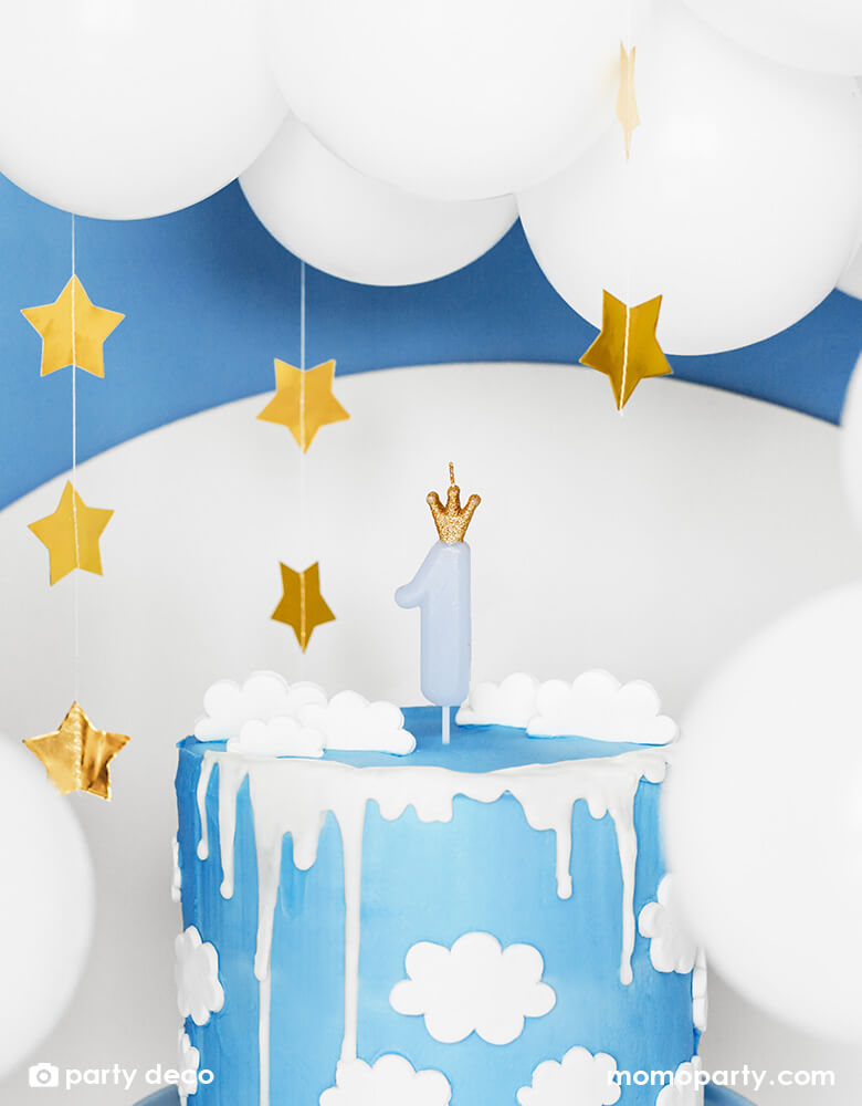 A blue birthday cake with cloud design on it which is topped with Momo Party's 3.5" blue Little Crown Birthday Candle by Party Deco, with star hanging garland in the back ground a beautiful white balloon cloud, it makes a prefect idea for a baby boy's first birthday party.