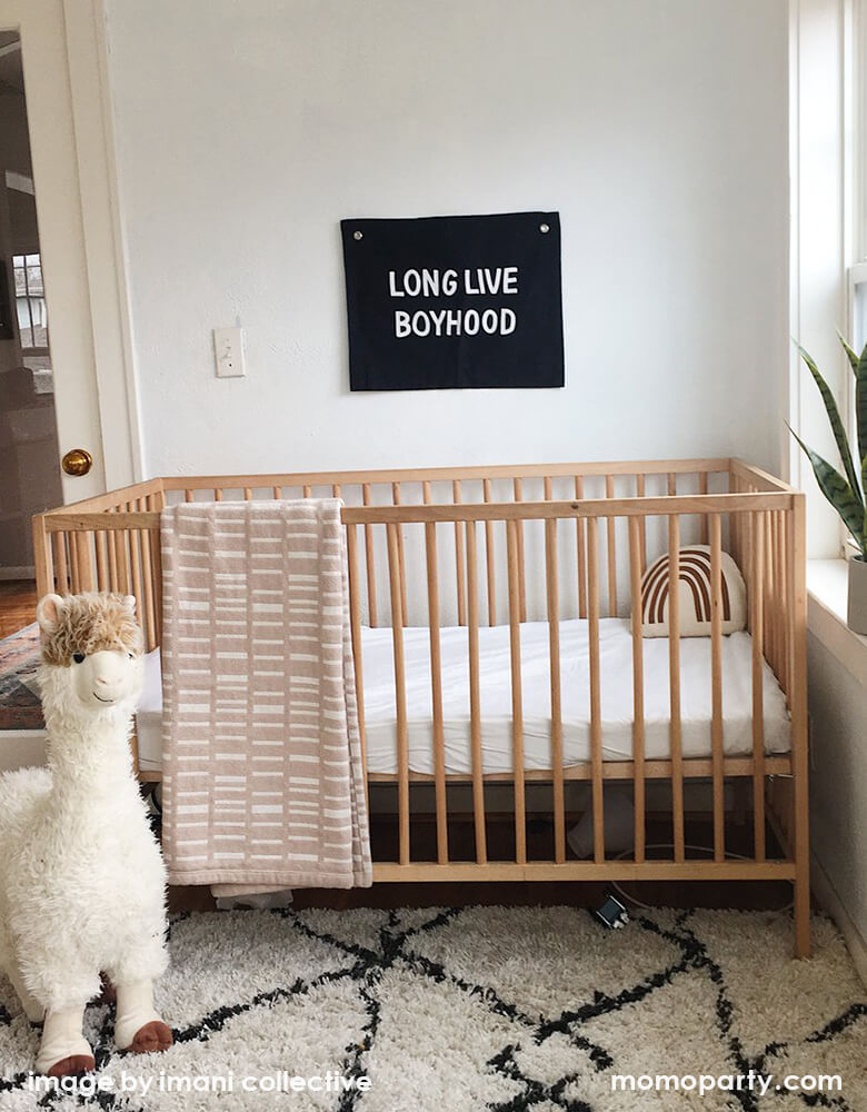 Imani Collective - Long Live Boyhood Banner. size 16 x 20 inches with 1/2 inch grommets. Black canvas with white screen print text. hanging on the wall with a wooden frame crib under it, a llama toy next to it.