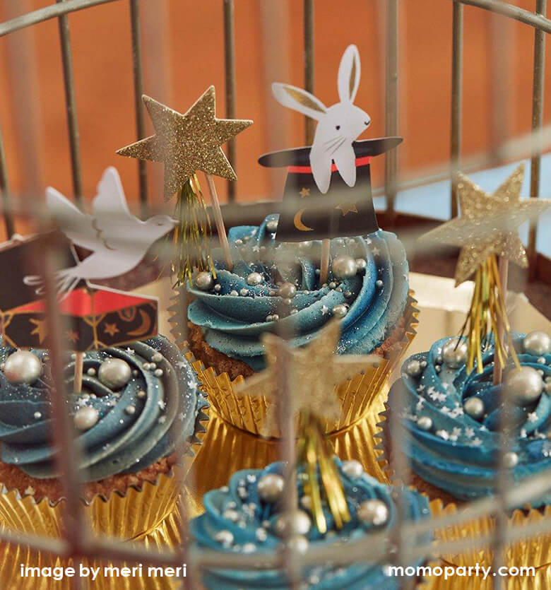 detail looks of Magic themed party, with cupcakes decorated Meri Meri Magic Cupcake Kit with gold glittering stars, cards, rabbits popping out of a hat and doves toppers inside a bird cage