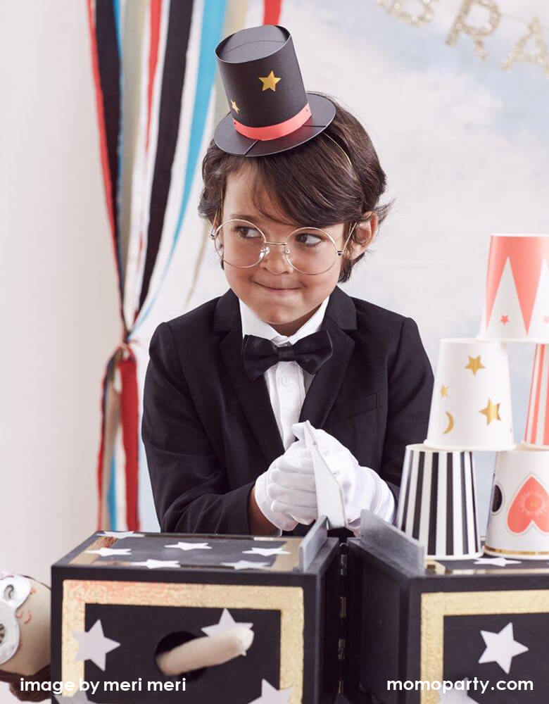 a bog dress up with a black tuxedo, wearing a Meri Meri Magician Party Hats and glasses, white glove playing a magic game in his magic themed birthday party.