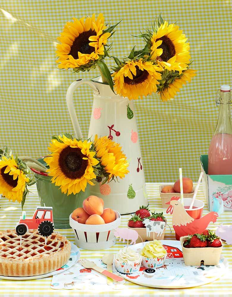 A farm themed party table with Meri-Meri's On-the-Farm-Collection_featuring farm themed party plates cups and napkins on a yellow gingham tablecloth