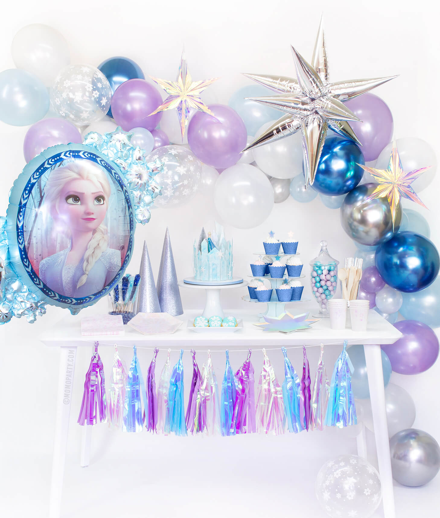 Momo Party Frozen Box, set up inspiration look with Frozen Balloon garland, with Jumbo 12 Point Silver Starburst Foil Balloon, Iridescent Star Decorations and  Disney Frozen 2 Elsa Anna Two Sided Foil Balloon as party backdrop wall decorations. Desert table with Meri Meri Shining Star Large Plates, Day Dream Society Frosted Small Plates, Iridescent Cups, Frosted Napkins, frozen cake with a elsa figure toy, for a modern Frozen party, Frozen 2 party, Girls Frozen birthday, frozen winter wonderland party
