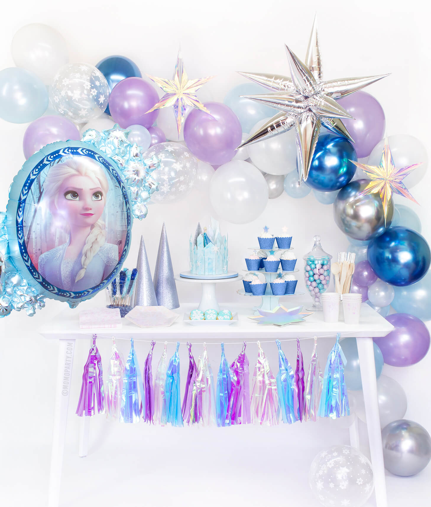 Momo Party Frozen Box, set up inspiration look with Frozen Balloon garland, with Jumbo 12 Point Silver Starburst Foil Balloon, Iridescent Star Decorations and Disney Frozen 2 Elsa Anna Two Sided Foil Balloon as party backdrop wall decorations. Desert table with Meri Meri Shining Star Large Plates, Day Dream Society Frosted Small Plates, Iridescent Cups, Frosted Napkins, frozen cake with a elsa figure toy, for a modern Frozen party, Frozen 2 party, Girls Frozen birthday, frozen winter wonderland party