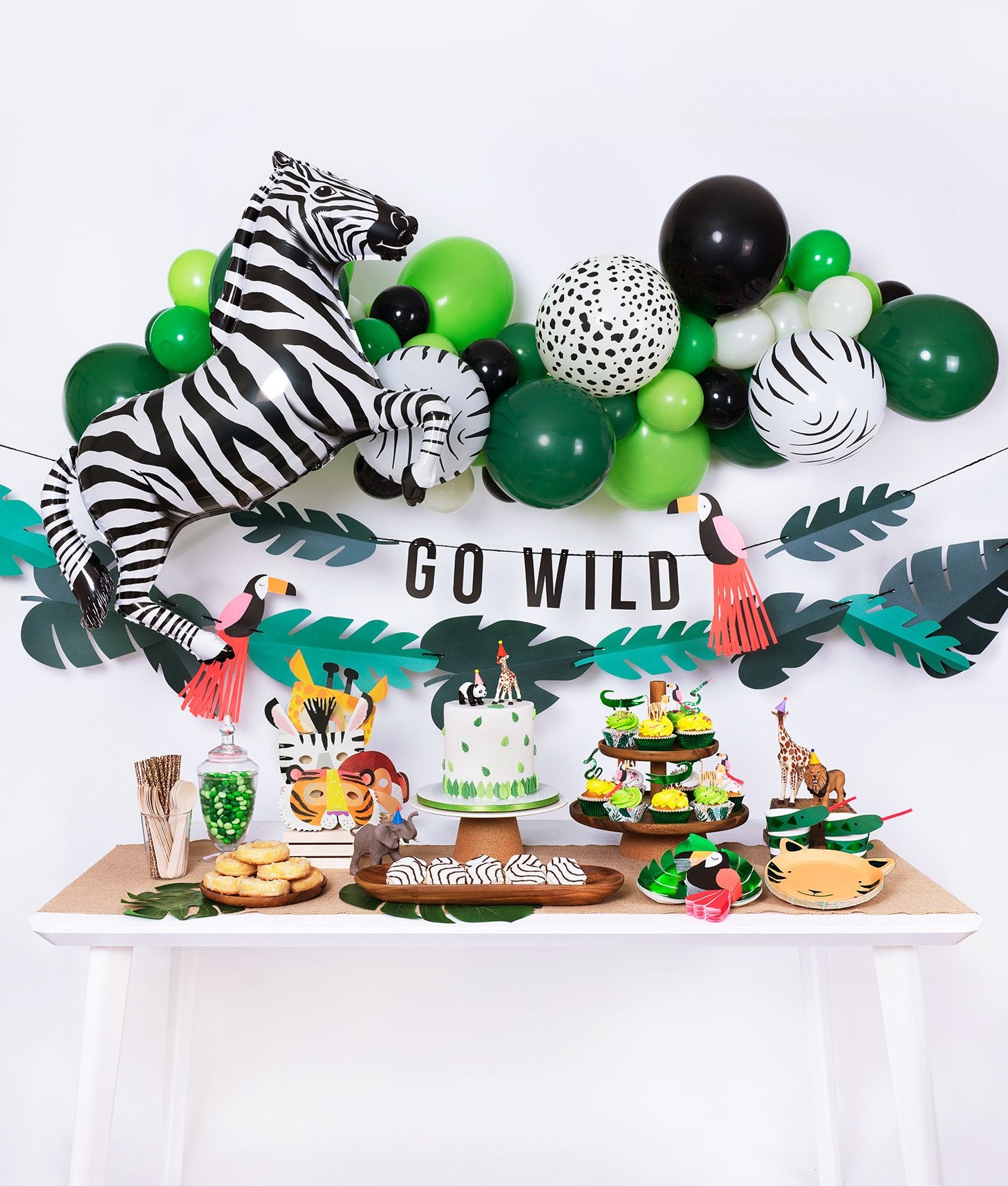 Momo Party jungle themed birthday party box with animal print balloon garland, zebra foil balloon, go wild garland decoration and tiger plates, tucan napkins, green foil plates, cake, cupcake, animal mask for kid's safari themed inspiration 