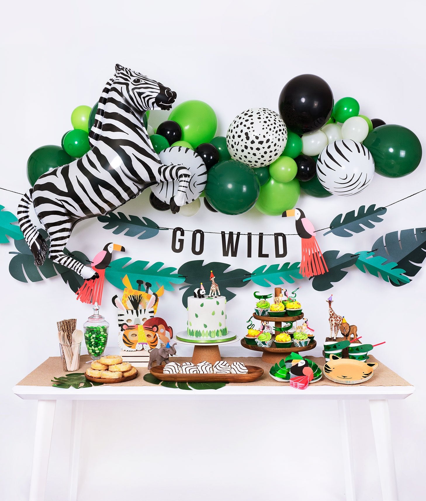 Momo Party jungle themed birthday party box with animal print balloon garland, zebra foil balloon, go wild garland decoration and tiger plates, tucan napkins, green foil plates, cake, cupcake, animal mask for kid's safari themed inspiration