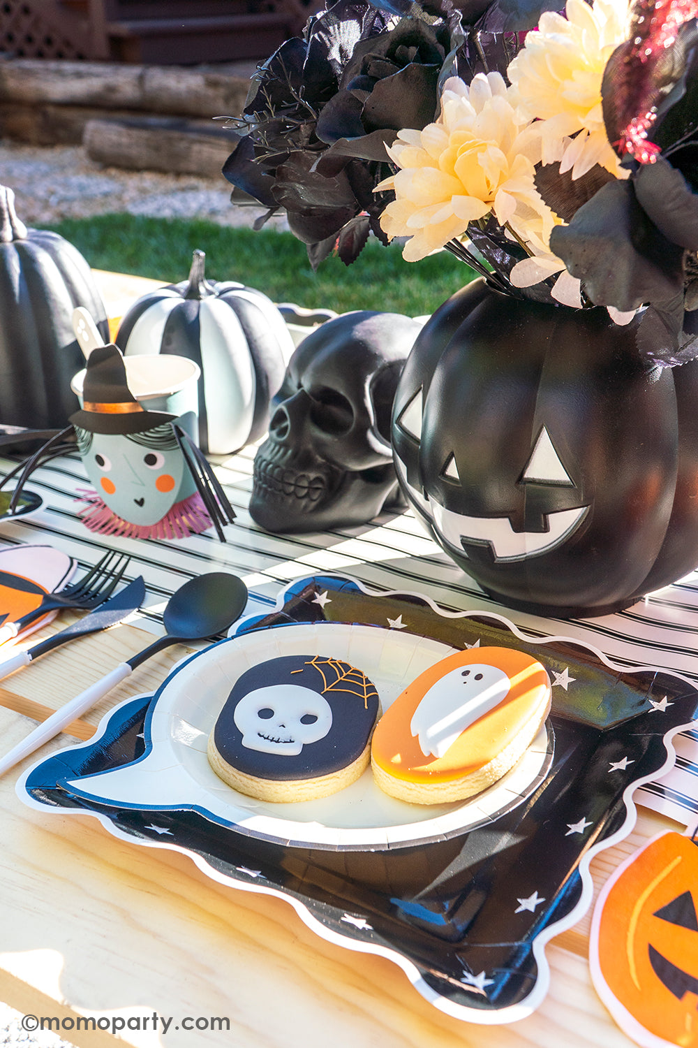 A spooky fun kid-friendly Halloween tablescape featuring My Mind's Eye's Night Sky Scalloped plates, Happy Haunting Boo Small Plates with had two matching Halloween themed sugar cookies on them, along with Jack o' Lantern pumpkin bucket shaped napkins and Meri Meri's Vintage Halloween party cups, on My Mind's Eye's black and white striped table runner, all makes a spook-tacular Halloween celebration inspo!