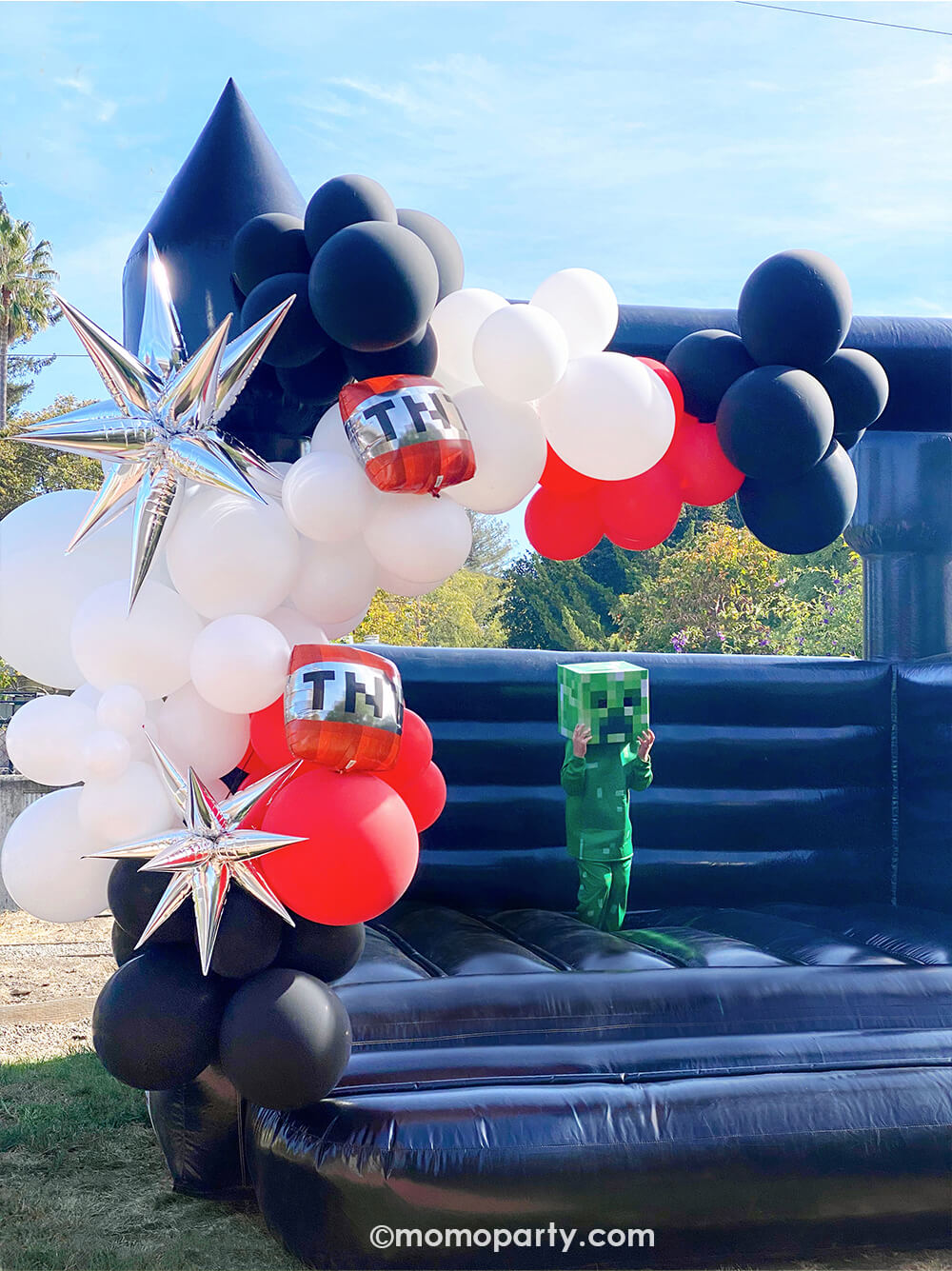 A modern Minecraft-themed birthday party by Momo Party. Featuring a giant black bouncing house adorned with black, white, and red latex balloons, 12 Point Silver Starburst Foil Balloons, and TNT foil balloons. A kid in a Creeper costume jumps with joy, making it a perfect and modern fun birthday party for boys.