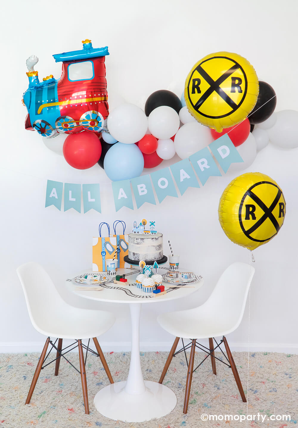 Momo Party Train themed party set up with a choo-choo-train-foil-balloon with classic train balloon garland hanging on the wall, RAILROAD CROSSING SIGN FOIL BALLOONs on the side, a light blue letter board spelled in "all aboard", a white rounded table filled with STEAM TRAIN SMALL PLATES, STEAM TRAIN CUPS, STEAM TRAIN CUPCAKE TOPPERS on the cake and cupcakes, train tape decorated the table top. Such a cute set up for a train themed birthday party, thomas the train birthday party, boy's birthday party