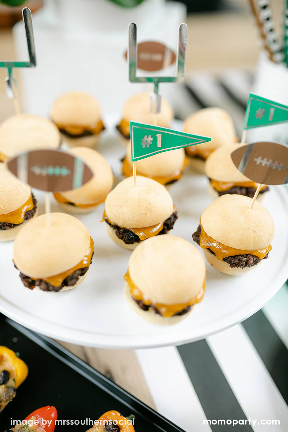 Details of American Football Party dessert table, mini burgers with cakewalk true brands Assorted Tailgate Treat Picks as small bits, on top of the a cake stand, with Hester & Cook simple black and white striped table runner. These modern table styling are perfect for super bowl party and entertaining with family and kids