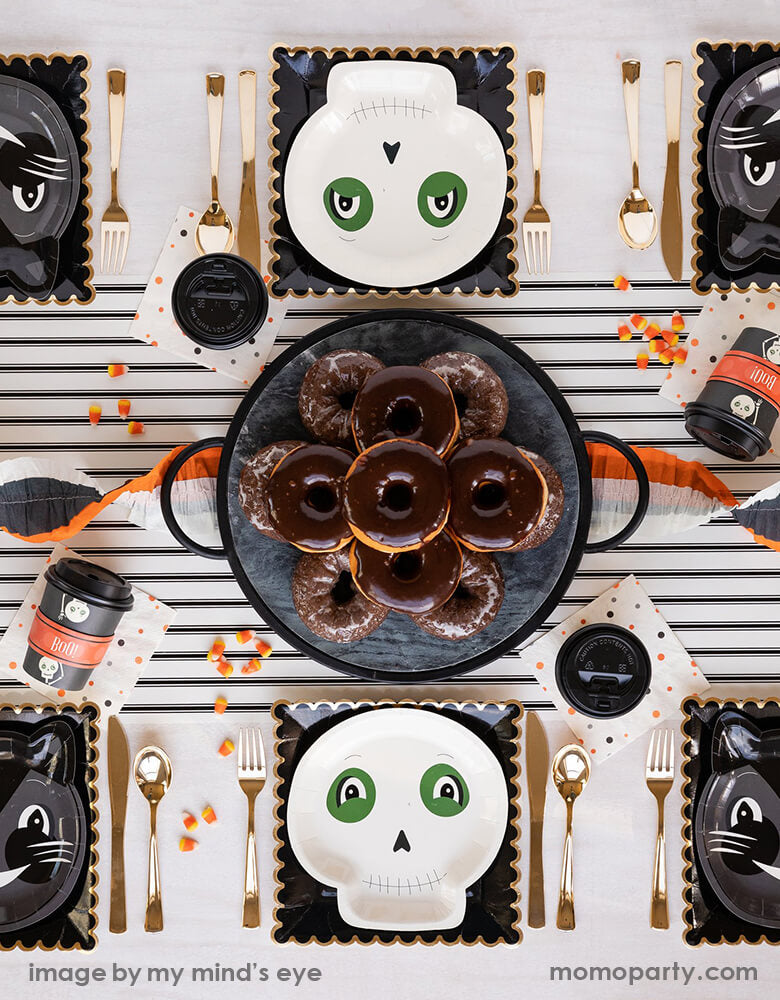Classic vintage halloween party 6 guest table set up, with vintage halloween cat plates and SKELETON plates layered with 9 inch black scallop plates, golden untils, vintage polka dots napkins. A Cream with Black Stripe Table Runner in the middle of the table with donuts on the cake stand in the center piece. Such a vintage fun halloween party look for a kids friendly halloween party