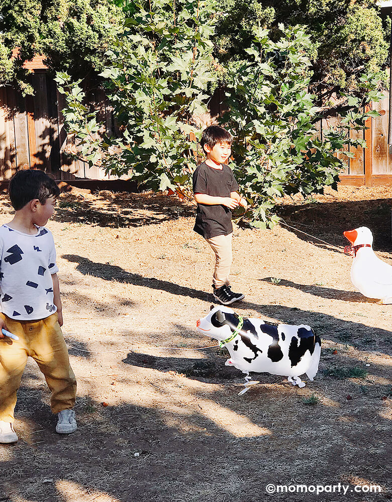 Boys walking a Cow My Own Pet Air Walker Foil Balloon and a Goose Cow My Own Pet Air Walker Foil Balloon in the backyard, the unique balloon design just like walking with a farm animals in a Kid Farm birthday party.
