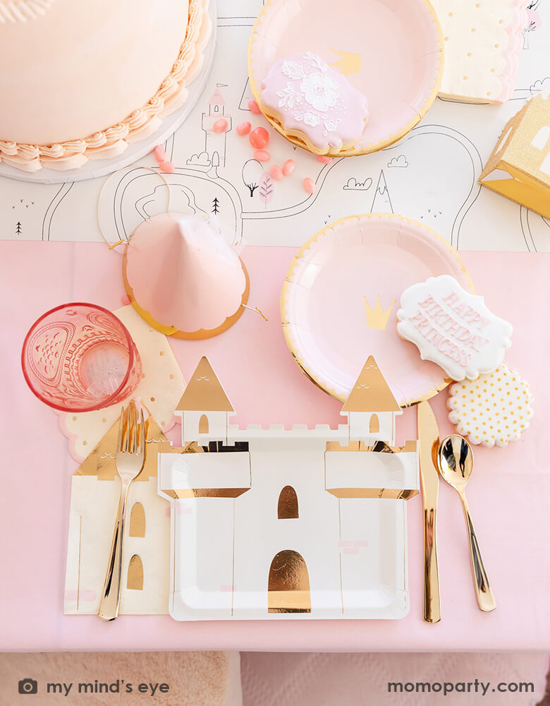 A beautiful tablescape from a girl's princess themed birthday party featuring Momo Party's princess castle shaped large plates, pink princess crown round side plate, turret shaped napkins, a pink princess birthday hat with tulle, in the middle it's a table runner featuring coloring princess fairytale illustrations, all in all makes a great inspiration for kid's princess themed birthday party.