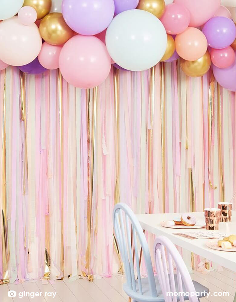 A beautiful pastel themed party with Ginger Ray 9.84 ft pastel streamer and balloon garland backdrop hung on the wall next to a pastel table/chair set, an easy yet show-stopping set up idea for weddings, girls' birthday party, bridal shower and baby shower