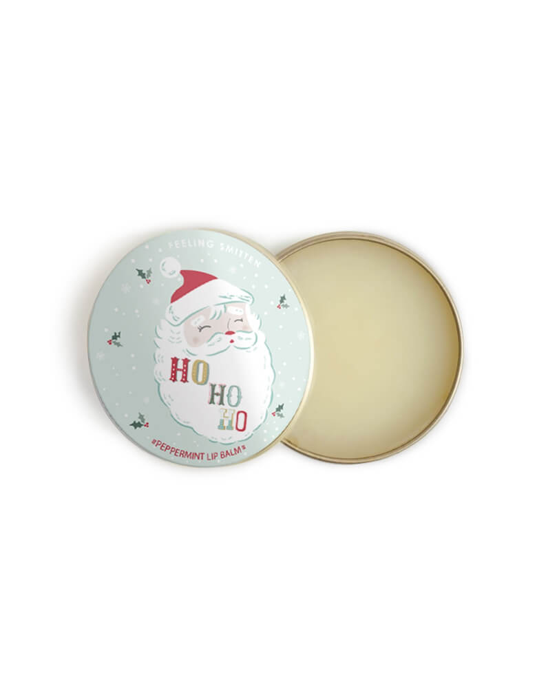 Feeling Smitten - Peppermint Santa Lip Balm. Featuring featuring beeswax and shea butter in a small rounded tin with Santa graphic and HOHOHO text on it. The weather outside may be frightful but your lips will feel delightful with this vanilla-kissed lip balm, naturally hydrate and protect against dry skin. use yourself or kid, sent it as gift to your loved one, it also a perfect for stocking stuffers