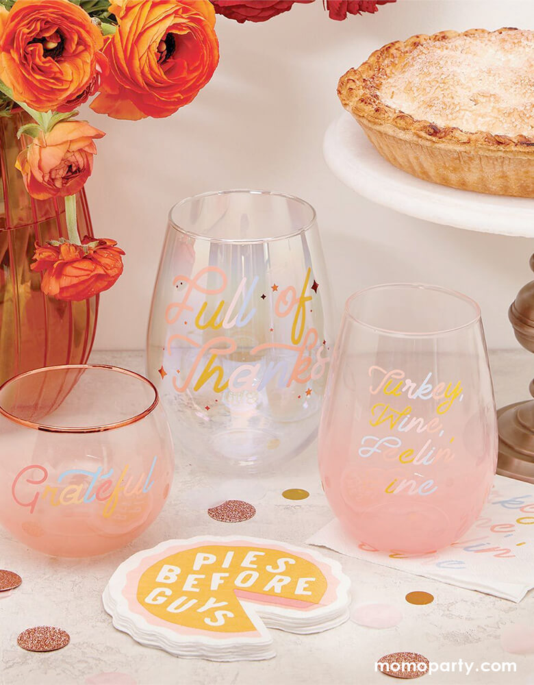 A girly friendsgiving party table with Pies Before Guys Napkins, wine glasses with "grateful" script design, and "full of thankful" script design , a pie on a cake stand and fresh flowers in a vest. 