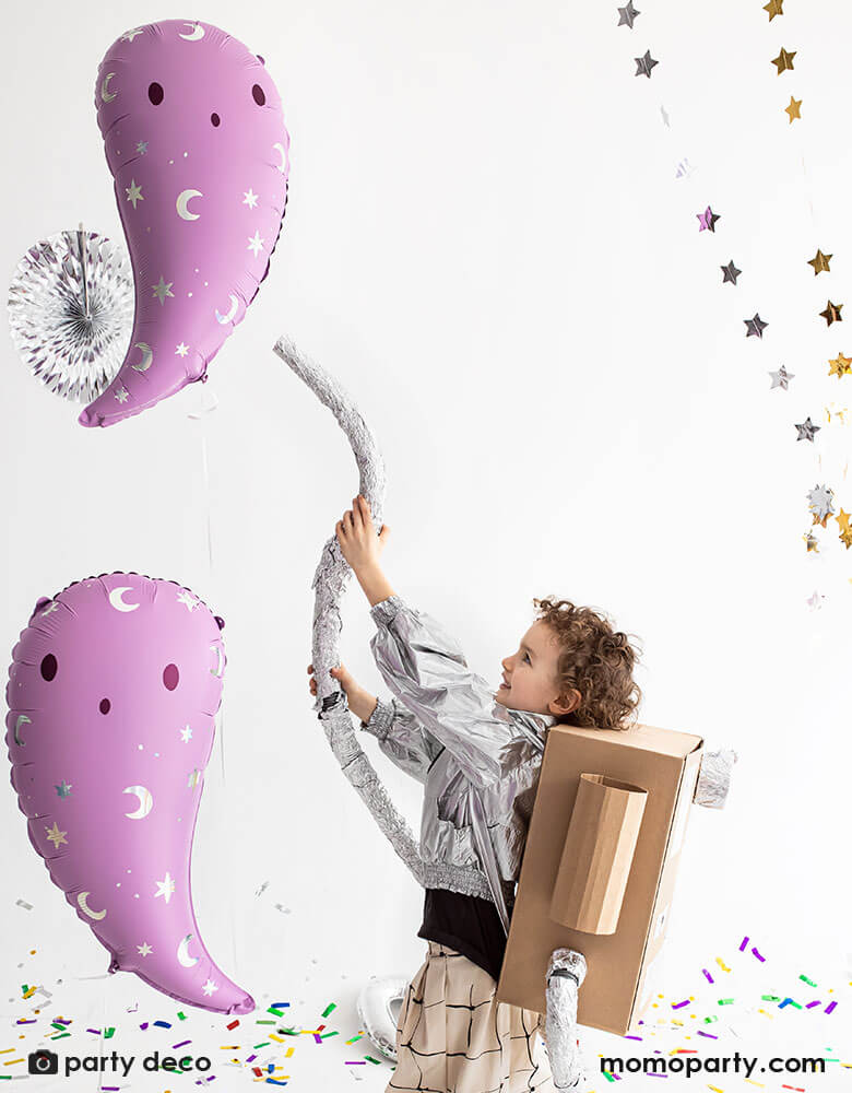 A little boy dressed up as the character from ghostbuster pretending to catch the pink ghost foil balloons in the air